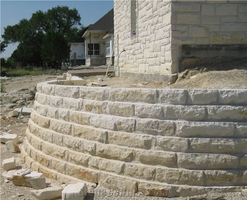 Curved chopped limestone retaining wall wrapping a slope beside a stone house