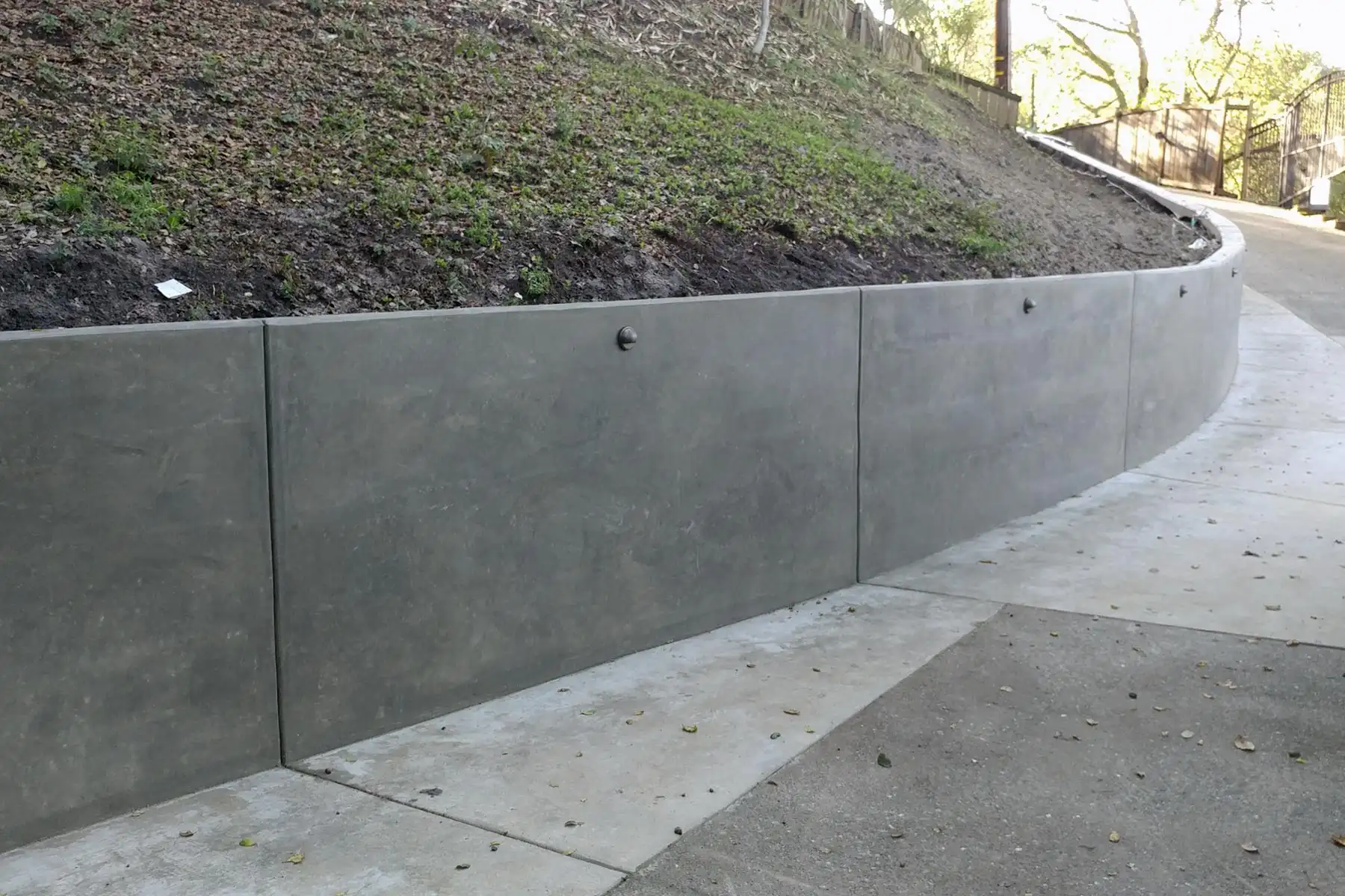 Smooth poured concrete retaining wall holding a slope beside a driveway