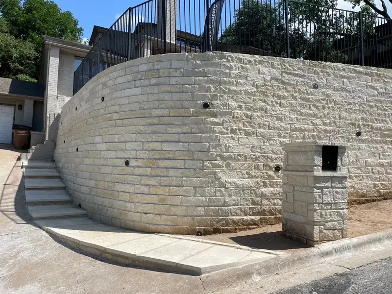 Tall curved limestone retaining wall with concrete steps climbing alongside