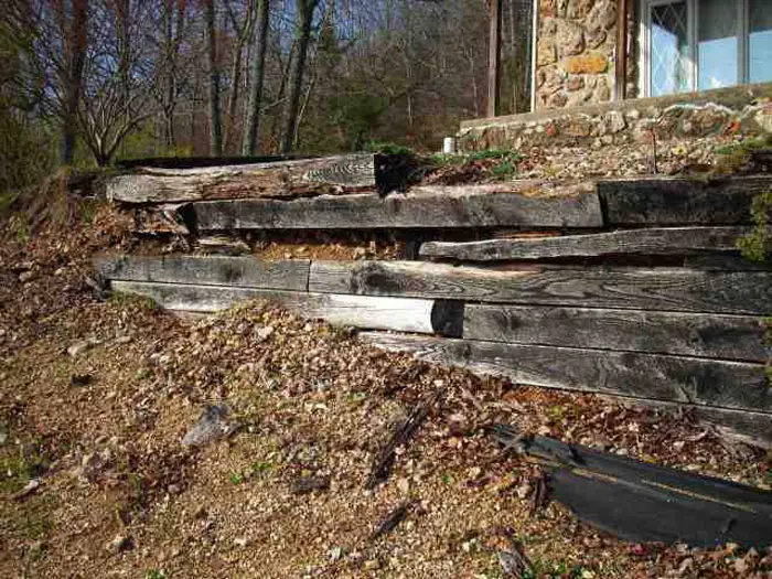 Old railroad-tie retaining wall rotting and slumping on a wooded slope