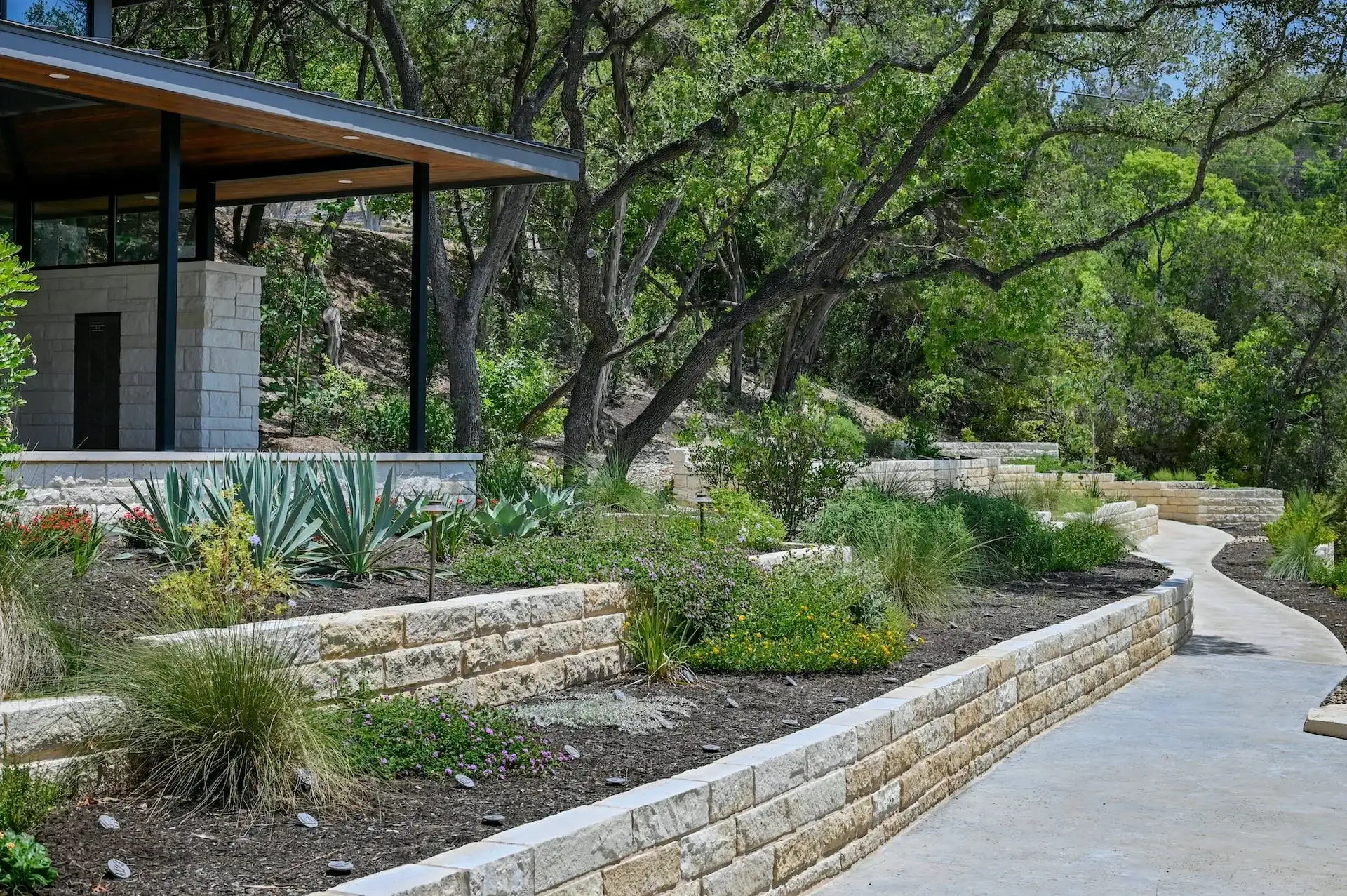 Limestone retaining wall and planted bed below a backyard pavilion under oaks